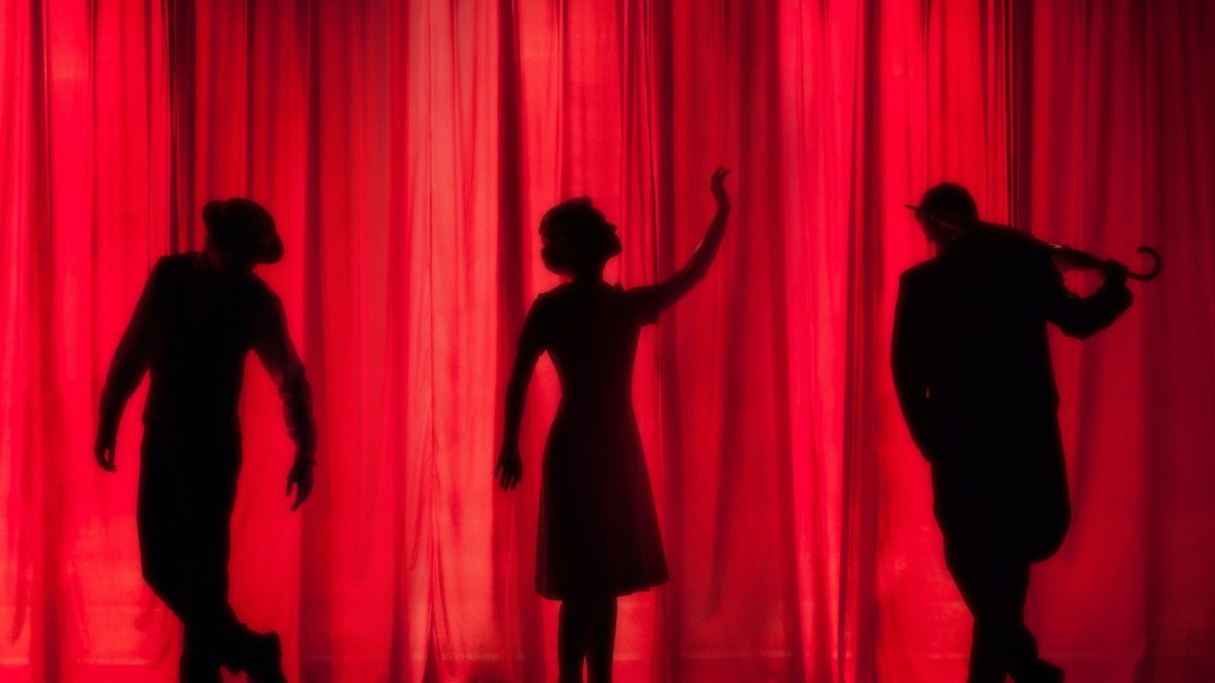 Three people behind a red curtain