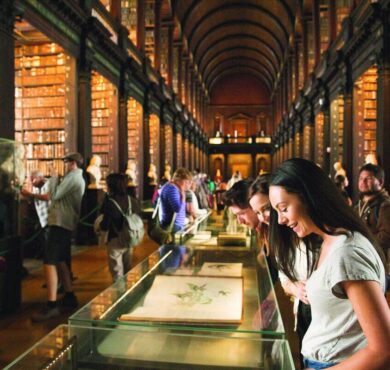 Guests exploring a grand library with high arched ceilings, historic books, and illuminated displays at luxury hotel.
