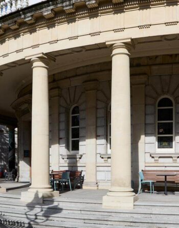 Elegant hotel facade with grand columns, outdoor seating, and historic architecture under a sunlit sky.