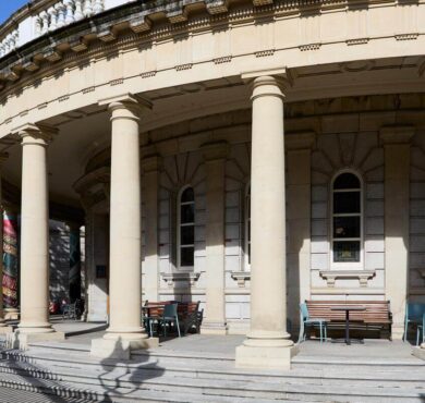 Elegant hotel facade with grand columns, outdoor seating, and historic architecture under a sunlit sky.