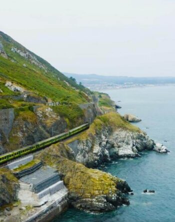 Scenic coastal view with train, lush green hills, and sweeping sea vistas near luxury seaside hotel, Ireland.
