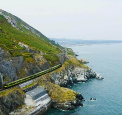 Scenic coastal view with train, lush green hills, and sweeping sea vistas near luxury seaside hotel, Ireland.