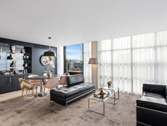 Elegant Spencer Penthouse Suite with spacious living room, balcony, queen bed, and deluxe amenities including robes, slippers, and umbrellas.