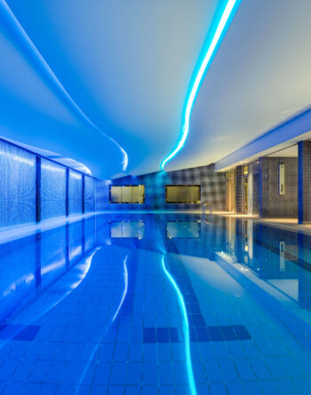 Luxurious hotel indoor pool with ambient blue lighting and relaxing lounge area, ideal for unwinding and leisure.