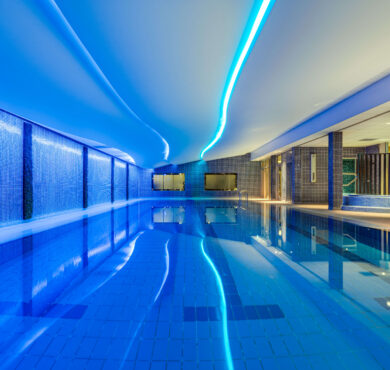 Luxurious hotel indoor pool with ambient blue lighting and relaxing lounge area, ideal for unwinding and leisure.