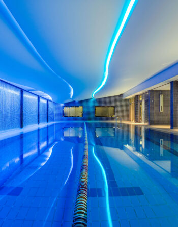 Luxurious indoor swimming pool with ambient blue lighting and sleek tiles at upscale hotel.