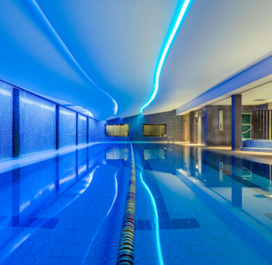 Luxurious indoor swimming pool with ambient blue lighting and sleek tiles at upscale hotel.