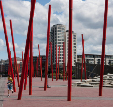 Guests enjoy biking and strolling near modern red sculptures against urban backdrop and cloudy sky, Dublin city centre.
