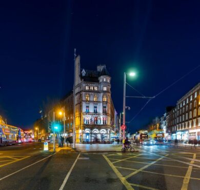 Elegant hotel facade at night, surrounded by vibrant city lights and buses, offering central accommodation and nightlife access.