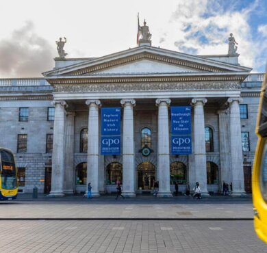 Grand historic hotel façade with classic columns and nearby city buses, inviting atmosphere for exploring Dublin.