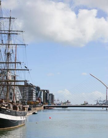 Riverside view with historic ship and modern bridge near city hotel, blending tradition and innovation for guests.