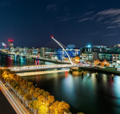Night view from hotel balcony of illuminated Samuel Beckett Bridge over River Liffey, riverside restaurants and city lights