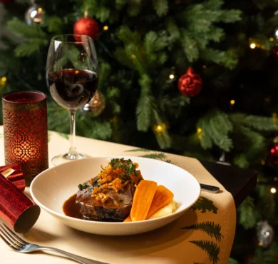 Festive plated roast with carrot, mashed potato, red wine and candle by a decorated Christmas tree in cosy dining.