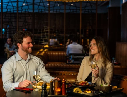 Couple enjoying evening hotel dining with wine, plated meals and cosy leather banquette in a dimly lit bar-restaurant